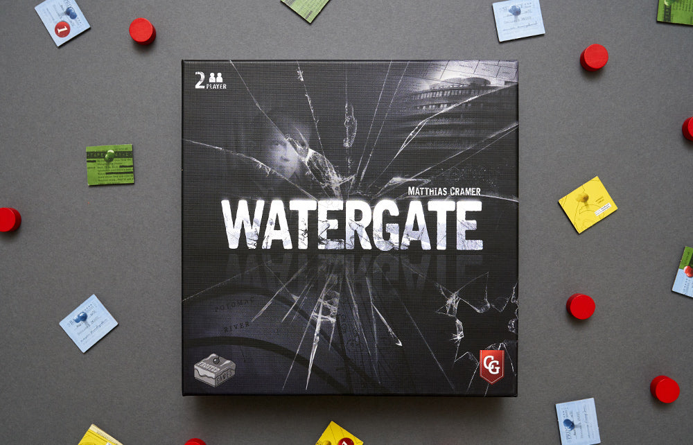 Watergate board game box by Matthias Cramer, featuring a dark cracked-glass design with the Capstone Games logo, surrounded by scattered game components.