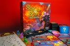 Slay the Spire: The Board Game box displayed upright alongside spread-out components including miniatures, player boards, cards, and tokens on a red background.