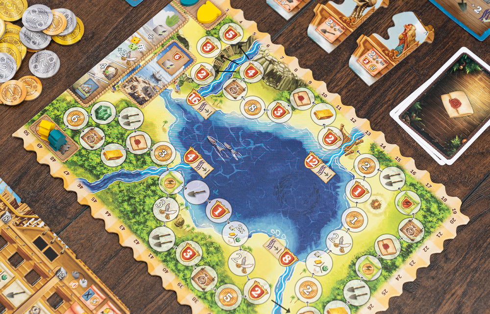 Pirates of Maracaibo in-play setup showing the island game board with numbered spaces, gold and silver coins, player tiles, and cards on a wooden table.