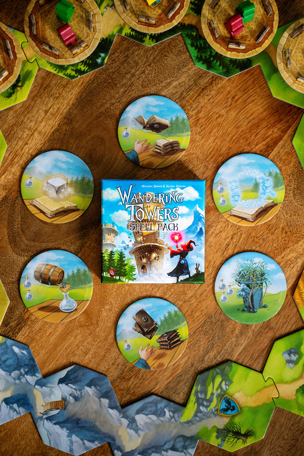 Wandering Towers Spell Pack box surrounded by circular spell tiles and hexagonal terrain tiles with wooden tower pieces on a wooden surface.