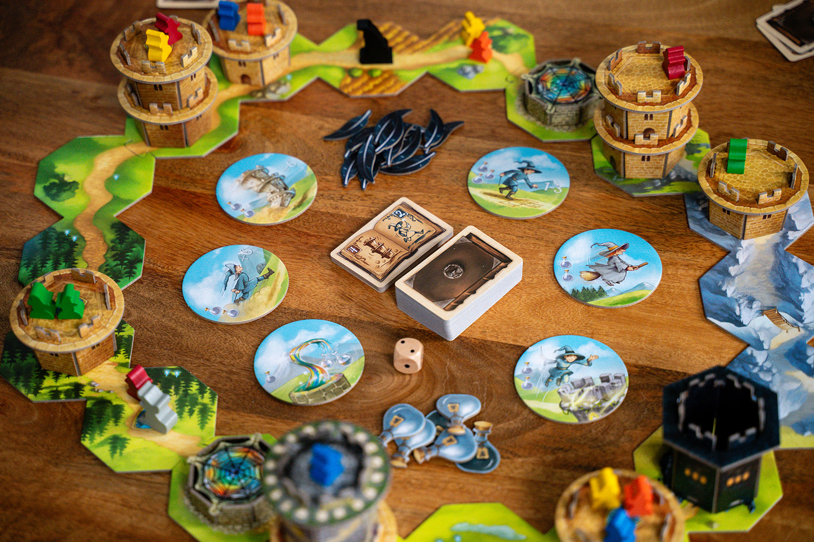 Wandering Towers board game mid-game setup showing 3D tower miniatures, hexagonal terrain tiles, wizard character tokens, card decks, and a die on a wooden table.