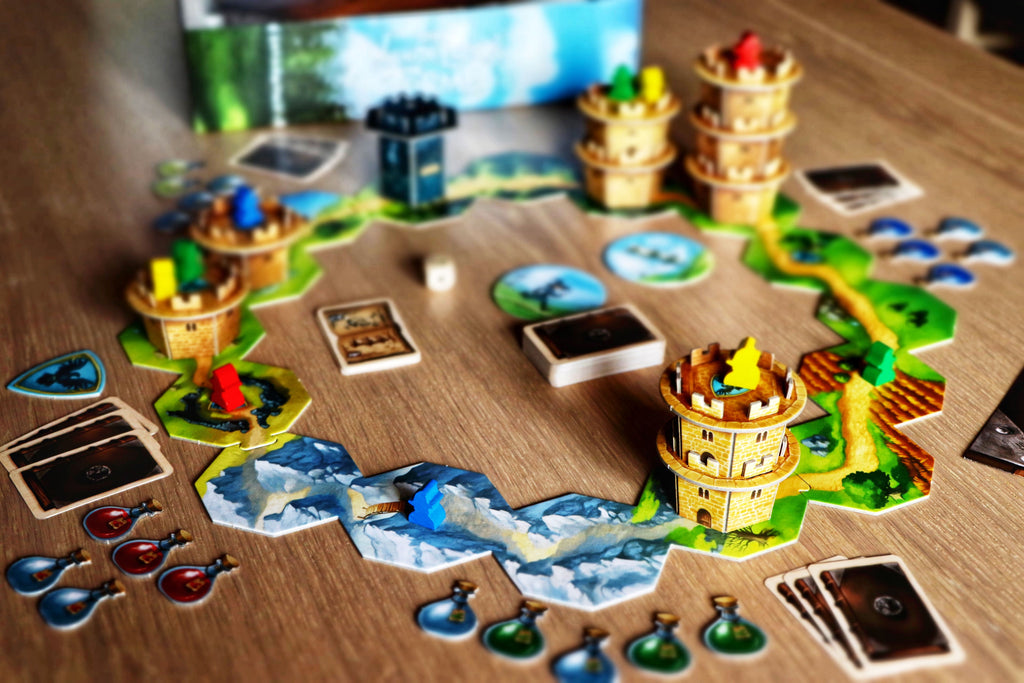 Wandering Towers board game set up on a wooden table showing 3D laser-cut tower miniatures on illustrated hex tiles with colorful meeples and potion tokens.