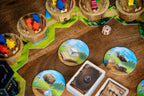 Close-up of Wandering Towers Spell Pack in play, showing 3D cardboard tower miniatures with colorful meeples, round spell tokens, cards, and a wooden die on a game board.