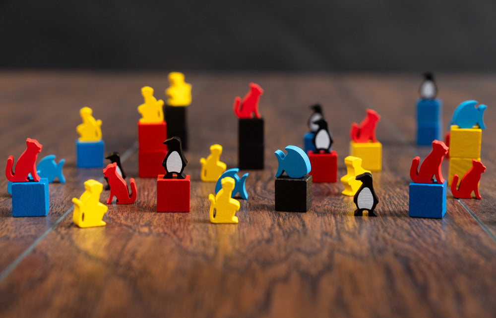 Colorful wooden animal meeples and cubes from Ark Nova Marine Worlds including cats, penguins, and fish in red, blue, yellow, and black.