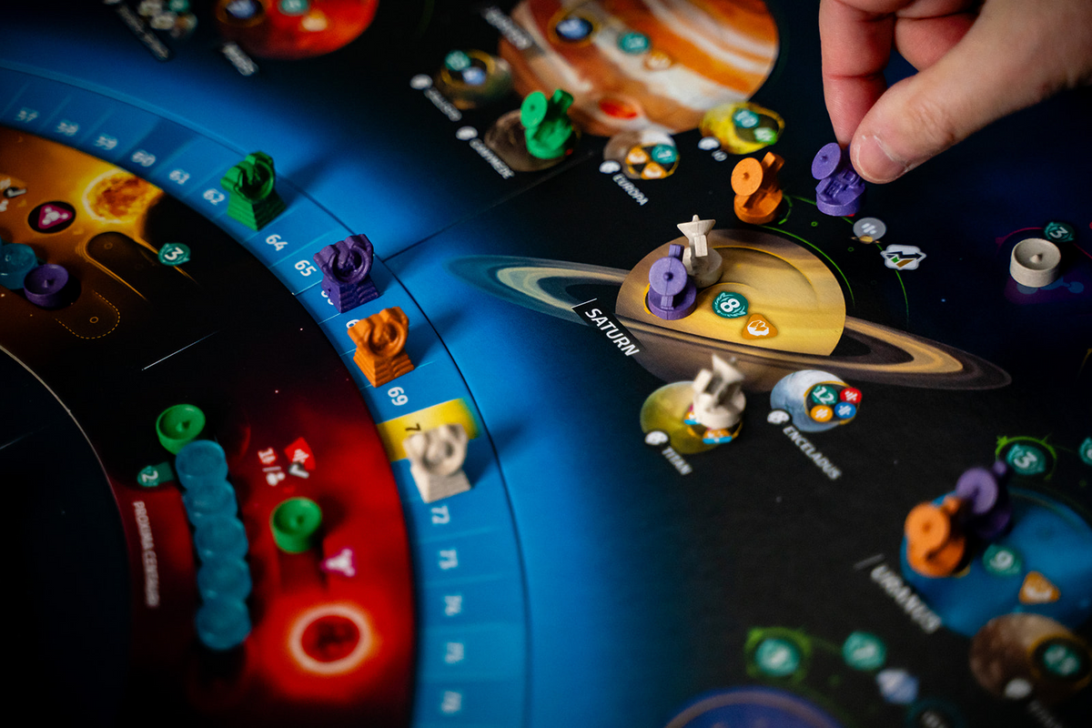 Close-up of SETI board game in play, showing colorful meeples and discs on a solar system board near Saturn and Europa.