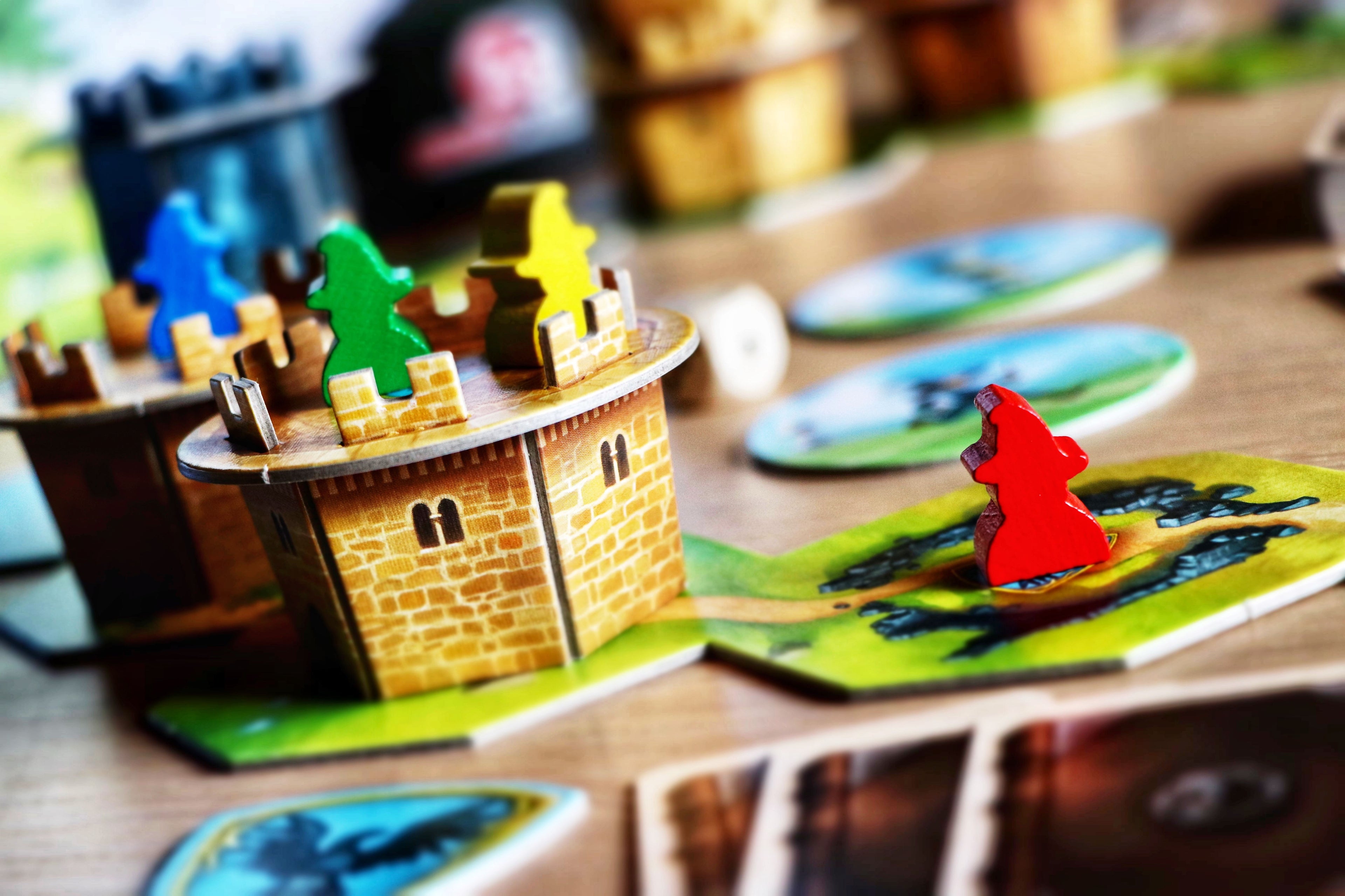 Wandering Towers board game close-up showing a detailed laser-cut wooden castle tower with colorful meeples and illustrated landscape tiles.