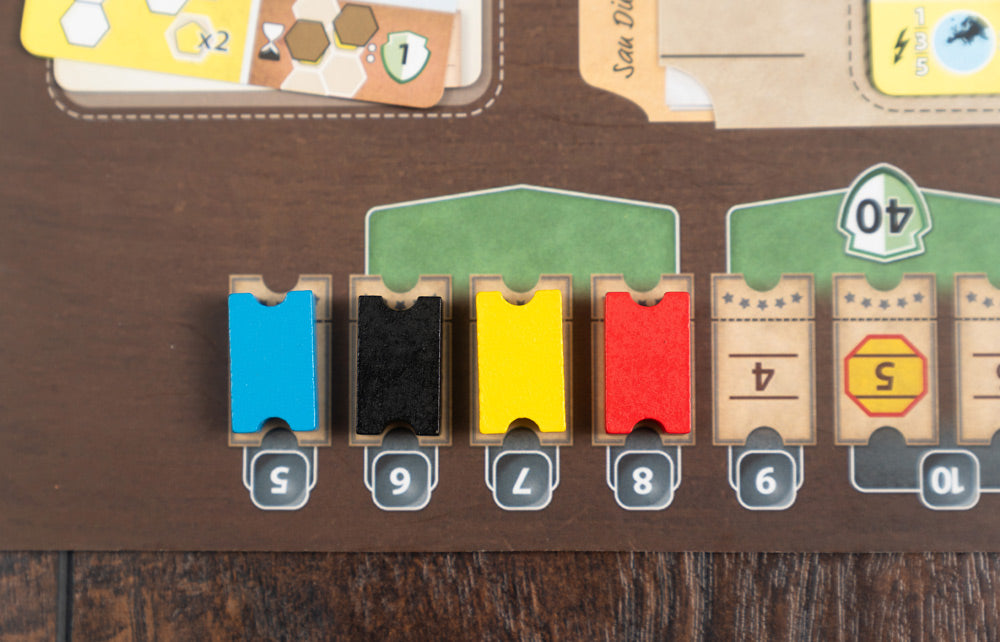 Close-up of Ark Nova Marine Worlds board showing colored wooden ticket tokens in blue, black, yellow, and red slotted into numbered card holders on a game board.